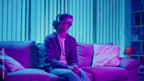 Mixed Reality, Future Technology, Mental Escape. Young Man Sits on Sofa at Night in AR Glasses, Interacting with Virtual Interface. Immersive Experience in Digital World of Tomorrow