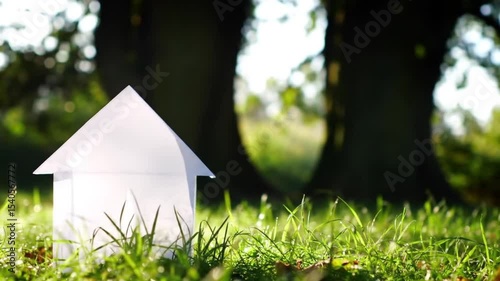 Small white paper house in grassy autumn woodland. Ideal for seasonal designs, real estate marketing, nature backgrounds, and conceptual art projects.