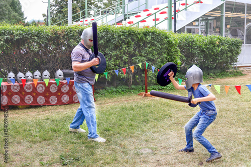 Canvastavla Father and child wearing helmets engage in a playful medieval sword fight with foam swords and shields