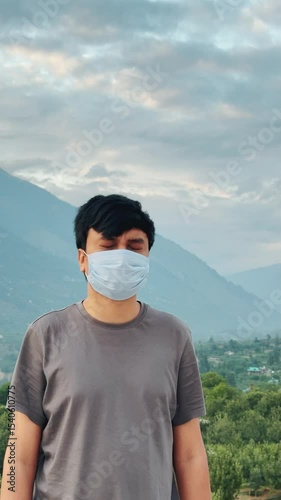 4K Vertical shot of an Indian man wearing face mask suffering from eye strain blinking his eyes while standing outside at Manali in Himachal Pradesh, India. Man suffering from eye strain stand outside