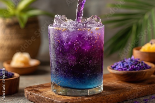 Refreshing butterfly pea flower tea with ice, a cool and vibrant summer drink, with sparkling bubbles, served on a wooden board, with fresh flowers in the background.