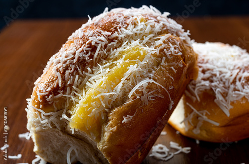 Sweet rolls with vanilla cream and grated coconut on a rustic brown wooden table and black background