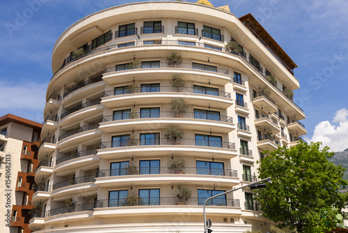 Modern apartment building with curved balconies and potted trees. Contemporary architecture, urban greenery, and residential luxury.