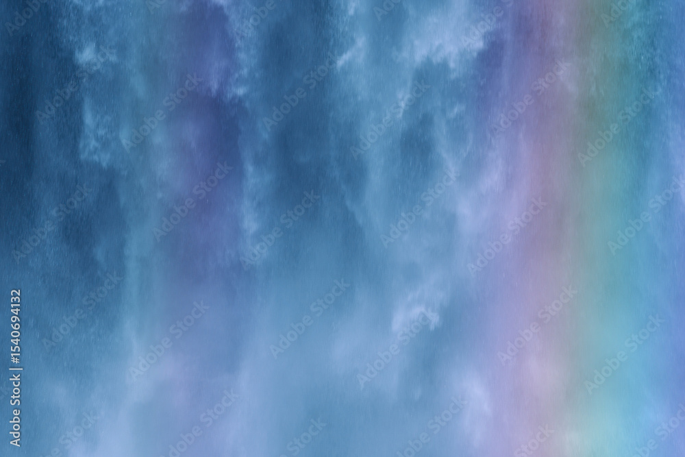 Obraz premium Water cascades down a rocky cliff, creating a vibrant mist that catches the sunlight and forms a rainbow