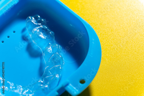 Close-up Blue plastic case with transparent brackets on a peach background. Invisible removable retainers for orthodontic treatment
