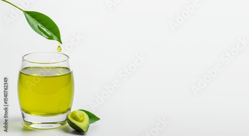 Fresh Avocado Oil in Glass - A glass of fresh avocado oil with a single drop falling from an avocado leaf. Half an avocado sits beside the glass on a white background