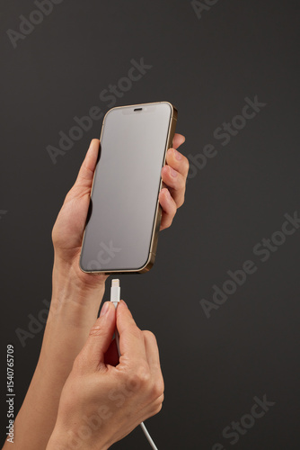 female hand connect charger cord into smartphone to charge battery on black background, Wired charging