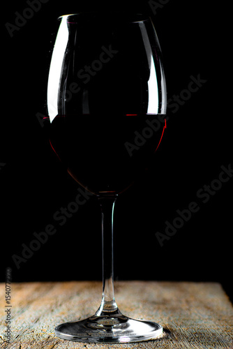 Obraz na plátně Taça de cristal com vinho tinto e garrafa sobre a mesa de madeira rústica, com fundo preto