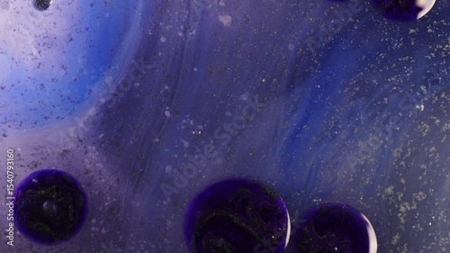 Closeup of deep violet and blue ink drops swirling and expanding in liquid. Bubbles and glitter particles enhance the ethereal, cosmic appearance.