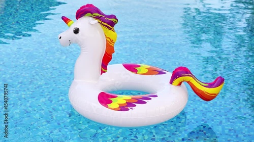 A delightful inflatable unicorn float, adorned with a rainbow mane and tail, rests serenely on the shimmering blue water of a swimming pool.
