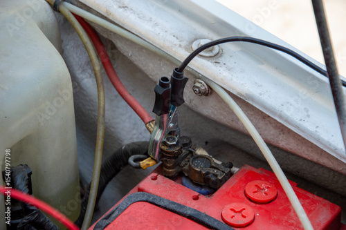 Technician connects a tester to the battery terminal while servicing a vehicle in a sunny outdoor environment