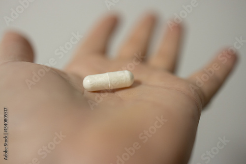 Hand holding single white capsule close-up focus on palm drug health care concept
