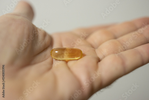 Hand holding single yellow gel capsule in close-up neutral background