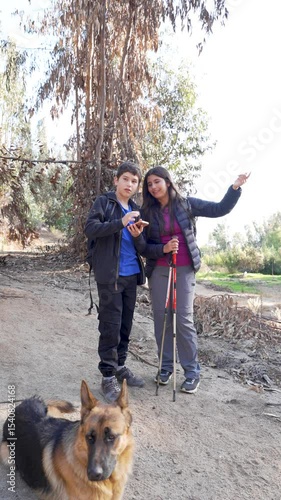 Two latin American young hikers consult a phone for directions, accompanied by their faithful german shepherd dog during a nature walk