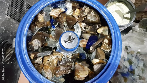 Stones rotating inside the bowl of a vibratory tumbling machine with white polishing powder Cerium oxide (CeO2)