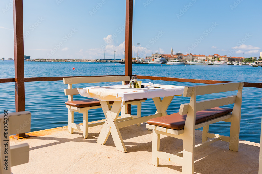 Fototapeta premium Outdoor cafe or restaurant with sea view and empty chairs. Coastal relaxation, summer tourism, and beachfront dining in the Mediterranean region.