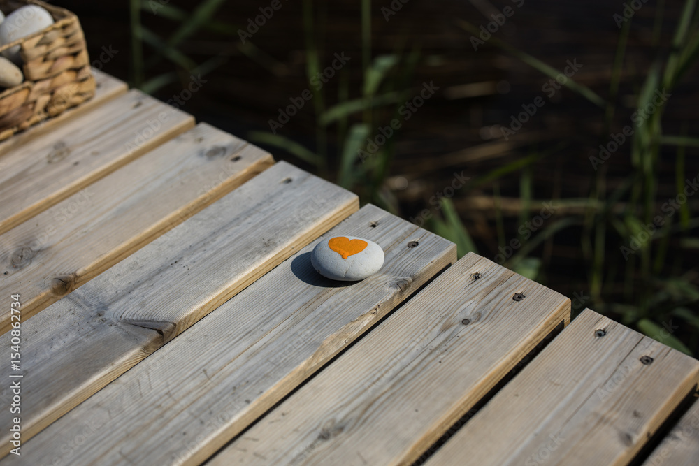 Fototapeta premium Tiny white rock with an orange heart painted on a pier during sunny summer weather