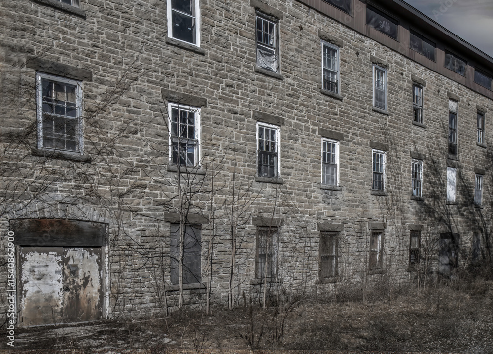 Fototapeta premium Old dilapidated grey stone building with boarded up windows in an overgrown field, nobody