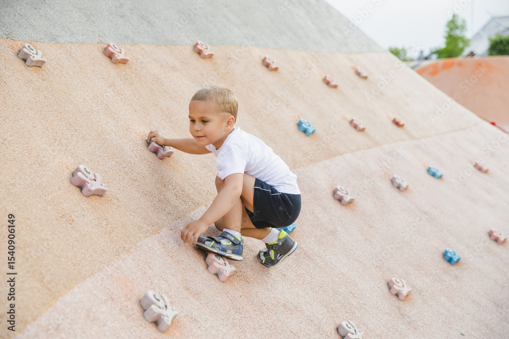Naklejka premium little boy climbing stone wall on playground. sport life concept