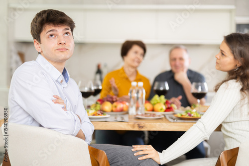 Dissatisfied guy turned away from the festive table, where his family and friends were having a conversation. Quarrel during home dinner photo