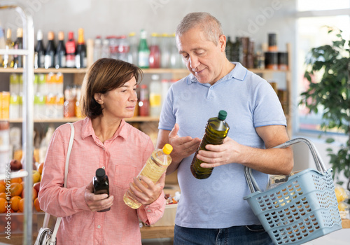 Couple of elderly man and elderly woman choosing olive or sunflower oil in bottle in grocery store