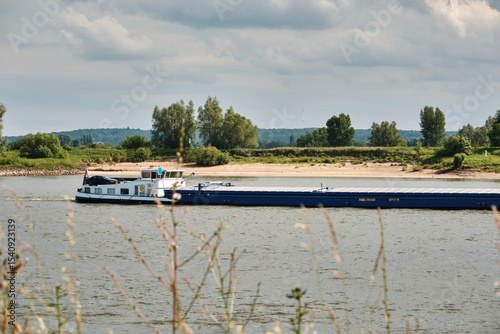 Cargo ship Natasja sailing downstream on the Rhine with green riverbank and sandy beach