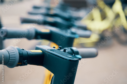 A row of electric scooters lined up on the street, showcasing their sleek metal frames and electric blue accents. The Bicycle handlebars and engineering design indicate a modern Machine construction