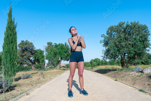 Mujer deportista con una quemadura en una pierna por el sol del verano y las manos en posición de rezo o súplica, un día soleado en el parque con cielo azul.