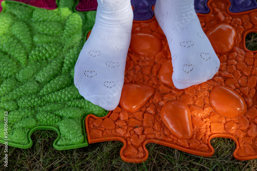 Wallpaper Mural Children's feet in white heart-patterned socks standing on a plastic puzzle mat for foot massage. 
 Torontodigital.ca