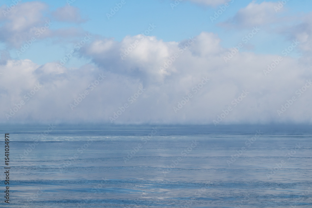 Fototapeta premium Frozen lake in winter with steamy puffy clouds on horizon