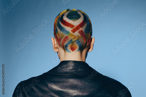 woman with colorful shaved hair design wearing black leather jacket against blue background, creative hairstyle, modern fashion, artistic expression, unique look