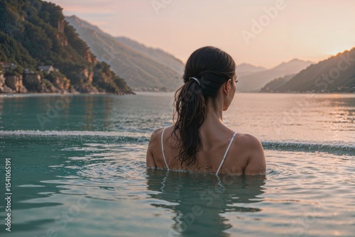 Woman swimming in mountain lake at sunset with scenic alpine landscape - luxury travel and outdoor adventure concept