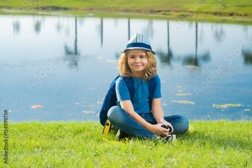 Child with binoculars travelling outdoors. Boy traveler with backpack in a summer day. Portrait of a little boy exploring wildlife. Hiking and adventure concept.