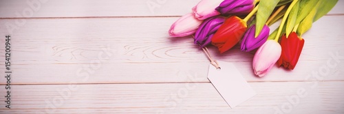 Flat design showing fresh tulips lying on pale wooden plank surface with blank gift tag resting