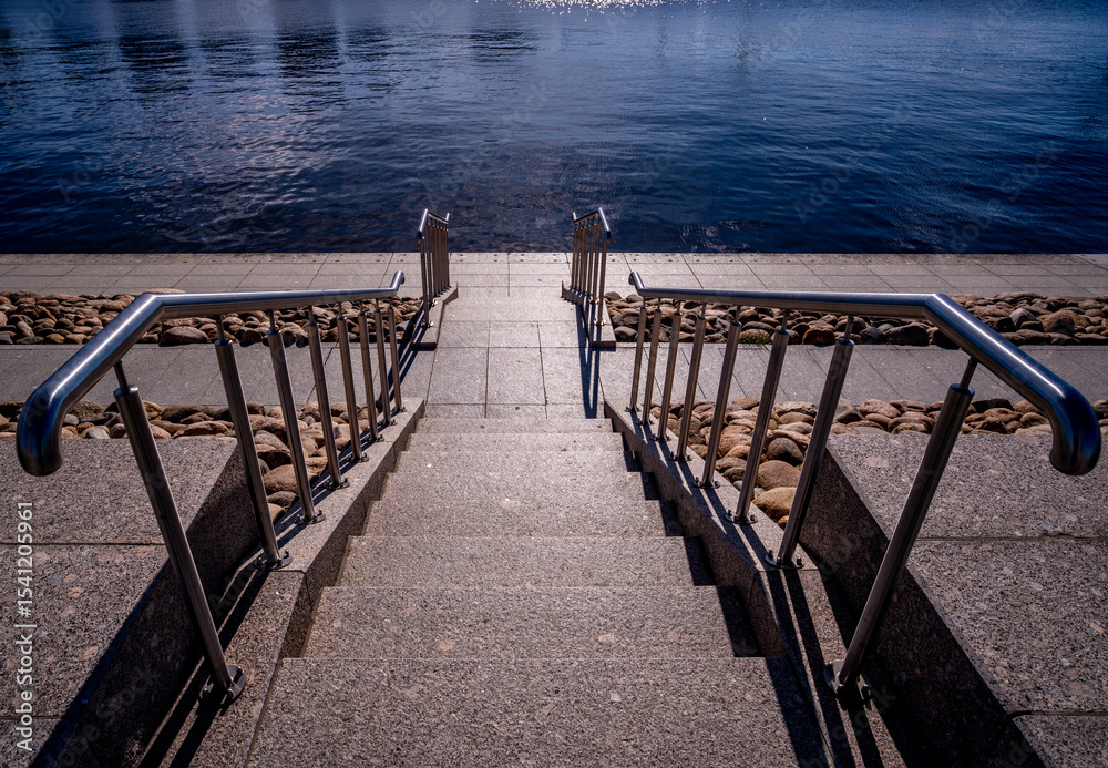 Obraz premium A stone staircase with a handrail leads to the water in the sea.