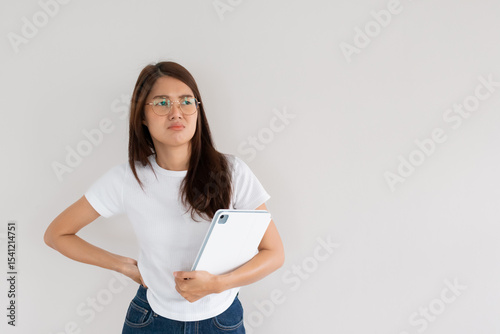 Asian Thai woman holding tablet and resting hand on waist with suspicion face, isolated over white wall