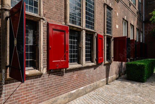 Historic Dutch Building with classic red wooden shutters on a windows. The brick facade and large windows with small panes are typical architectural elements of the Netherlands.