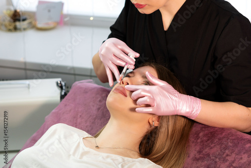 Beauty specialist administers lip filler injection during treatment. Aesthetic cosmetology. Lip Augmentation. Female client during procedure in beauty clinic
