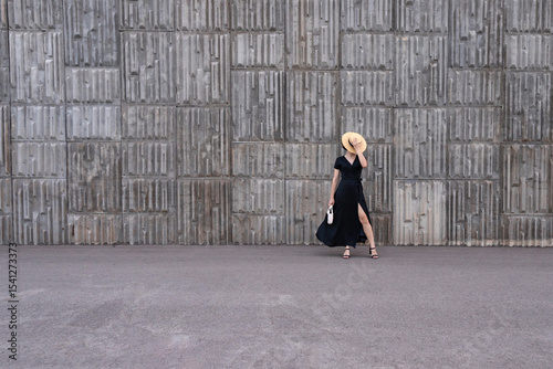 Woman in black polka-dot dress posing against concrete wall.