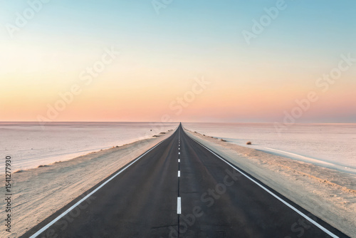 Endless asphalt road through desert salt flats at sunset