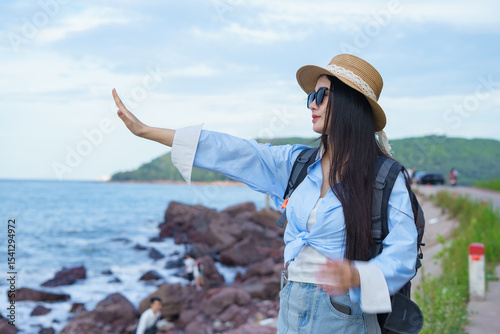 Young woman enjoying a coastal viewpoint with a hand gesture towards the sea at a scenic location during daytime