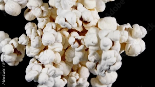 Freshly popped popcorn fills the frame in a close-up macro shot on empty black background. Fluffy white kernels with golden brown accents create a delicious texture. Concept of snack food, movie time,