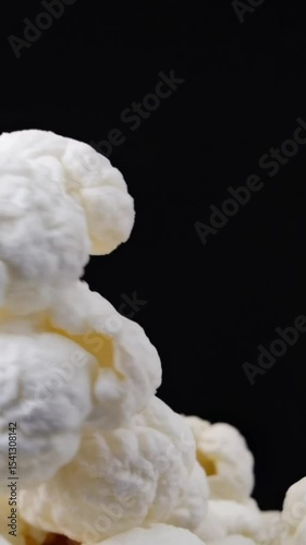 VerticalFreshly popped popcorn fills the frame in a close-up macro shot on empty black background. Fluffy white kernels with golden brown accents create a delicious texture. Concept snack, movie time,