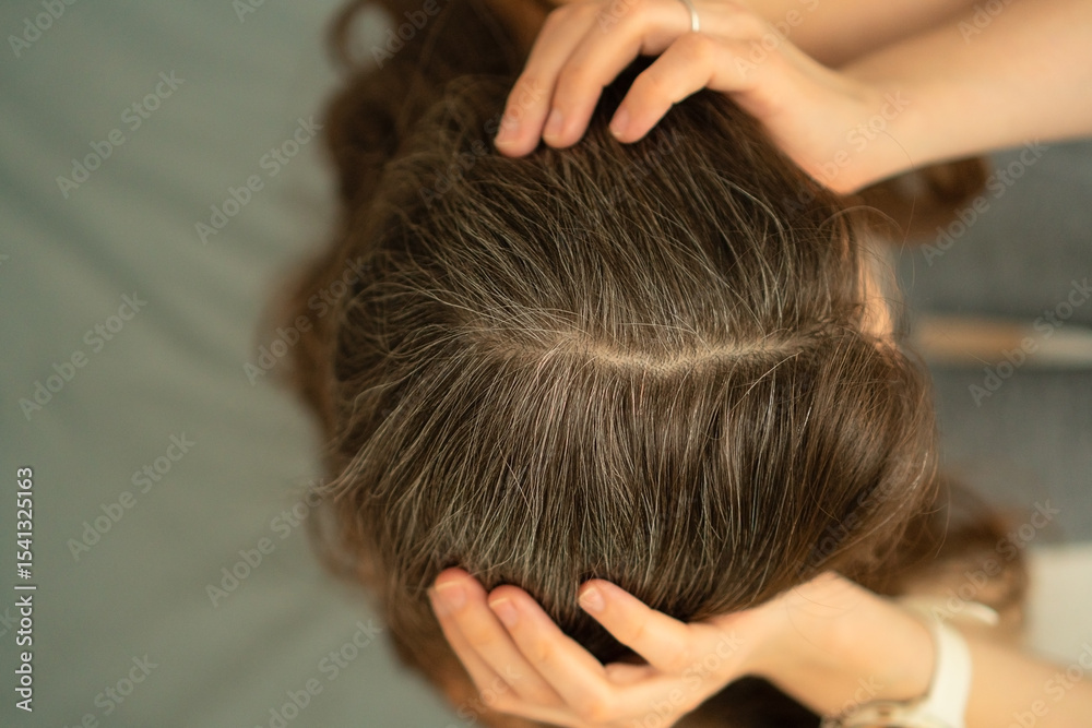 Fototapeta premium Close-up view from above of a woman touching her scalp and showing gray roots. Beauty in aging, self-acceptance, and gentle hair care. Natural transformation, soft light, healthy texture.