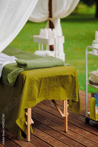 outdoor massage table with green linens set in serene garden atmosphere. wooden deck and white curtains enhance tranquil spa setting ideal for relaxation and rejuvenation photo