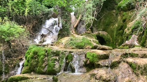 A waterfall with moss growing on the rocks. The water is crystal clear and the moss is green in color. The landscape is peaceful and serene.