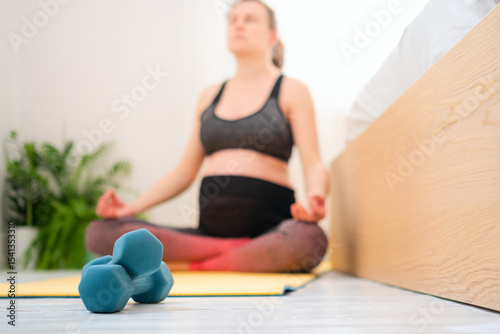 Close-up of dumbbells, pregnant woman training in the background. Light workout during pregnancy.