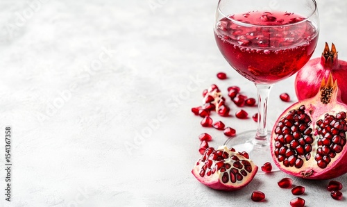 The image depicts a spotless white studio that includes a pomegranate alongside a full glass of its juice