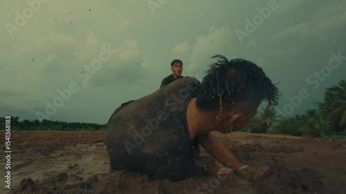 A football player fouls another in a muddy field, with a teammate helping up in slow motion
