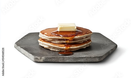 A black stone plate holds a neatly stacked pile of pancakes, topped with a butter cube and finished with a maple syrup drizzle, in this image